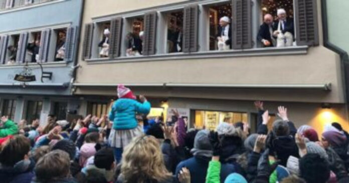 Zuenftler werfen an Baeckermoehli Essen in die Menschenmenge auf dem Kolinplatz in Zug 1