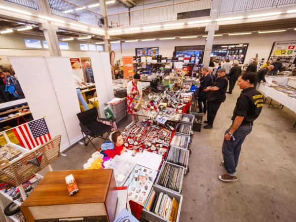 Autofans stehen vor einem flohmarktähnlichen Stand mit kleinen Gegenständen rund ums Auto.