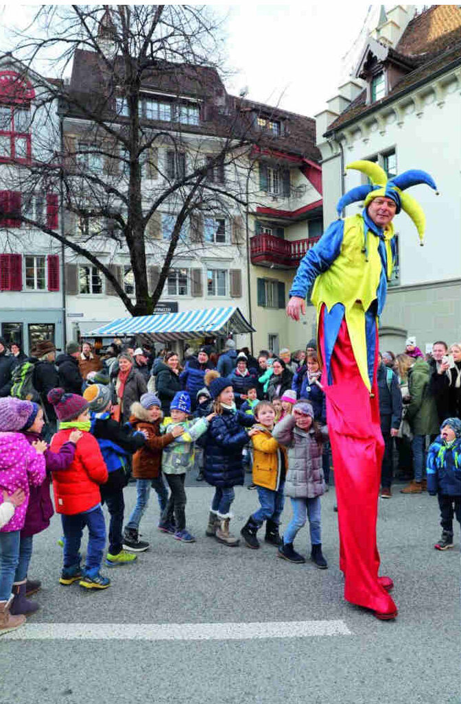 Ein Hofnarr auf Stelzen gefolgt von einer Kinderschar