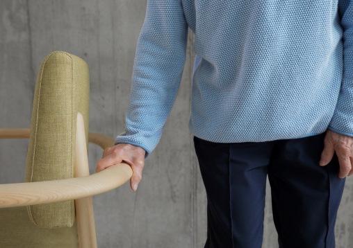 Eine ältere Person hält sich an einem Stuhl fest, dessen Design einen praktischen Griff aufweist.