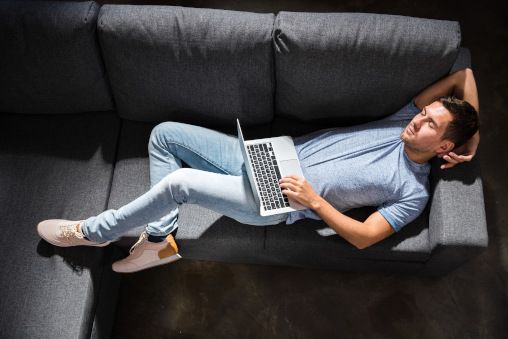 Mann liegt auf Couch, Laptop auf dem Schoss