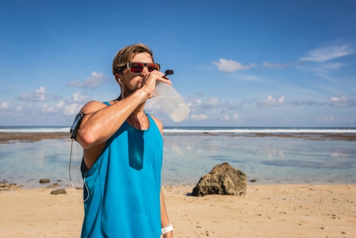 Mann trinkt Wasser aus einer Flasche am Strand