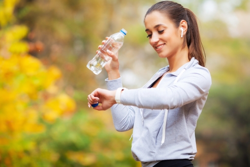 Joggerin hält Wasserflasche in der Hand und schaut auf die Uhr