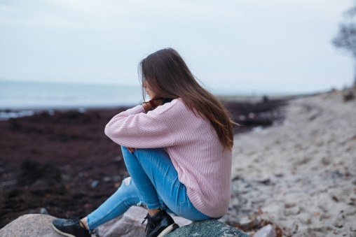 Eine deprimierte junge Frau sitzt am Strand