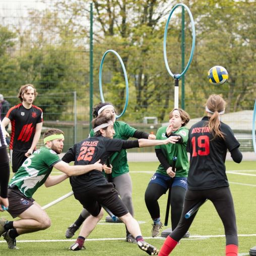 Quadballspieler werfen Bälle unter drei Ringen.