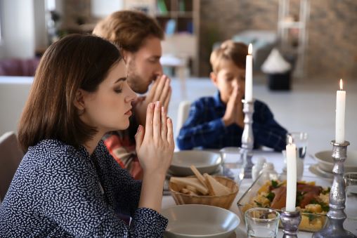 Familie betet vor dem Essen, jeder hält seine Hände über dem Teller zusammen.