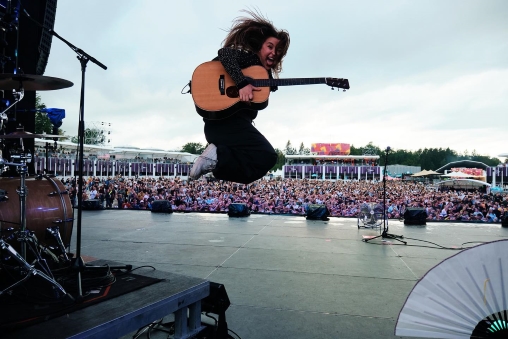 Joya Marleen springt an einem Festival auf der Bühne mit Gitarre in der Hand