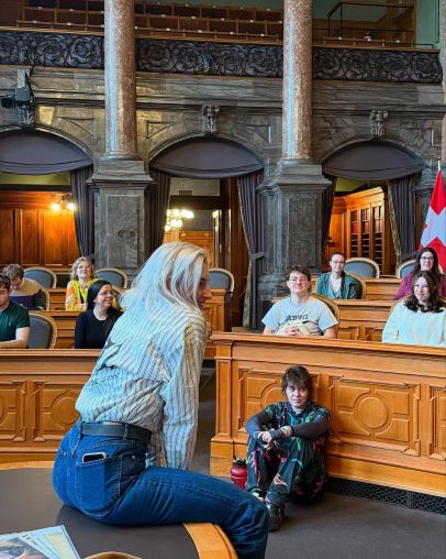 Anna Rosenwasser sitzt auf einem Tisch im Bundeshaus, umgeben von Jugendlichen.